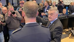 NRW-Innenminister und ein Polizist stehen vor mehreren Fotografen und Journalisten