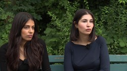 Zwei Frauen sitzen auf vor Gebüsch auf einer Bank
