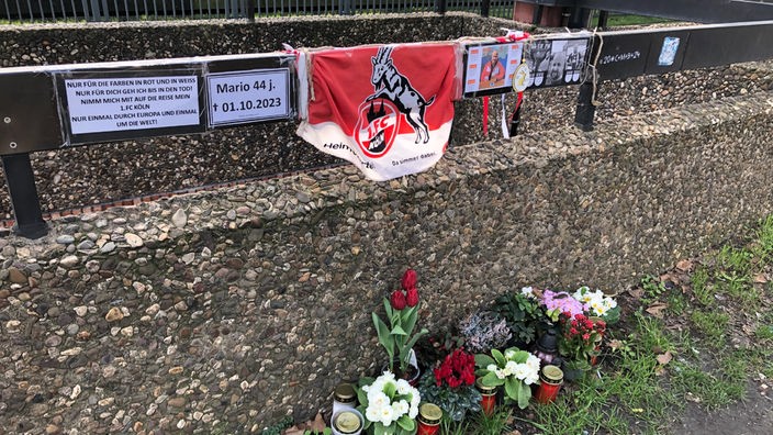 Der Gedenkort für den Fan, im Vordergrund liegen Blumen, auf einem Metallgelände hängen Fotos des Fans und eine FC-Flagge