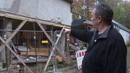 Mann zeigt Schäden, die drei Monate nach der Flut immer noch an seinem Haus zu sehen sind