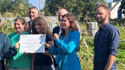 Sieben Personen halten eine Förderurkunde vor sich, sie stehen auf einem Feld