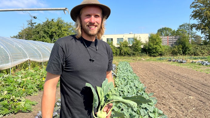 Linus Beste steht mit Gemüse in der Hand an seinem Feld