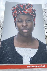 Das Bild zeigt das Porträt von Mutinta Hambiliki, einer schwarzen Frau. Sie trägt einen rot-schwarz-gemusterten Turban auf dem Kopf.