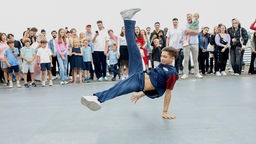 Ein junger Mann breakdanct auf dem Boden, um ihn herum stehen viele Zuschauer