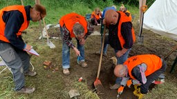Freiwillige in orangenen Westen graben in einer flachen Grube nach Relikten aus der Römerzeit