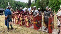 Als römische Legionäre verkleidete Personen stehen mit ihren Schilden, Waffen und Helmen in Reih und Glied. 