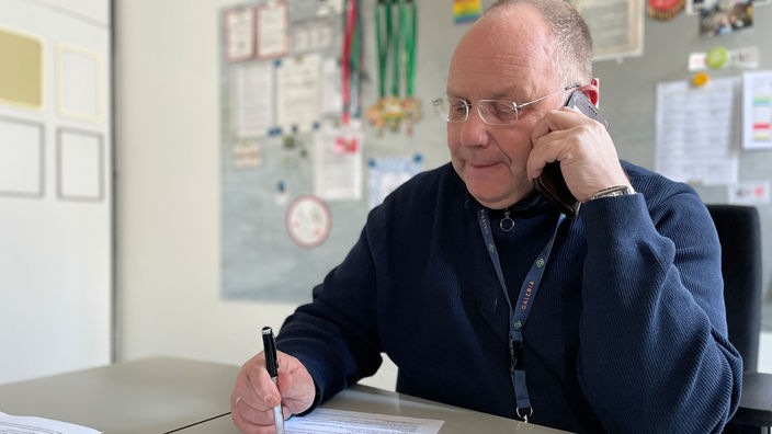Peter Zysik sitzt am Schreibtisch und telefoniert am Handy in seinem Büro in der Galeria-Fililale in Bonn