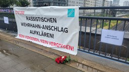Ein großes Banner und zwei Zitate an einem Brückengeländer befestigt, davor Rosen niedergelegt