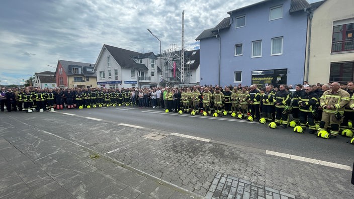 Eine große Gruppe von Leuten, in erster Linie Feuerwehrleuten, steht gemeinsam auf der Straße.