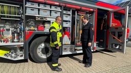 Zwei Feuerwehrleute stehen vor einem elektrischen Feuerwehrauto, Ausstattung zu sehen