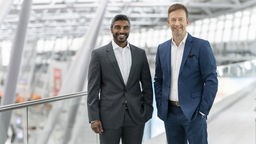 Lars Redeligx und Pradeep Pinakatt, die Geschäftsführer des Düsseldorfer Flughafens stehen im Flughafengebäude und lächeln in die Kamera.