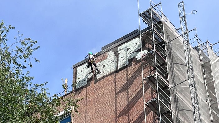 Ein Industriekletterer hängt an einem Seil und entfernt ein Graffiti an der WiSo-Fakultät der Uni Köln.