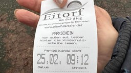Auf dem Bild ist ein Parkschein zu sehen mit der Aufschrift Eitdorf Parkzeitende 2073