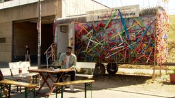 Hamzi sitzt vor einem mit bunten Bändern geschmückten Bauwagen.