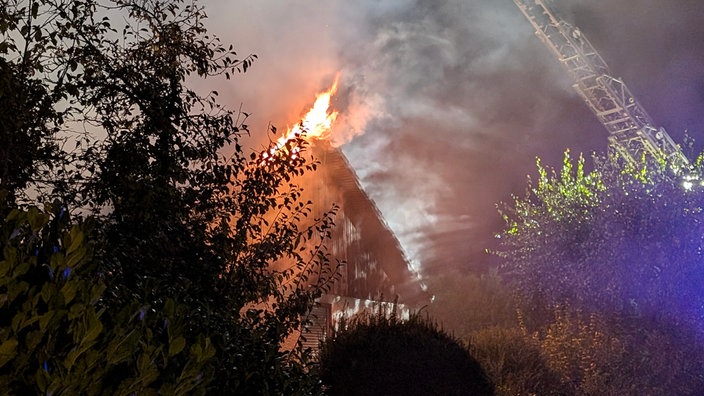 Ein brennendes Haus, aus dessen Dach Flammen lodern.