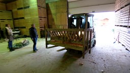 Auf dem Foto ist ein Traktor, der eine Futterkrippe aus Holz in eine Halle fährt.
