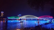 Die Hohenzollernbrücke leuchtet in grün, gelb und rot