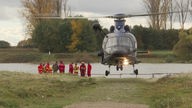 Hubschrauber steht am Rheinufer, daneben stehen Rettungskräfte