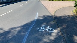 Auf dem Foto ist eine zweispurige Straße. Auf der rechten Seite ist ein Radweg mit einer etwas unsauber gezeichneten Linie von der Fahrbahn abgegrenzt.