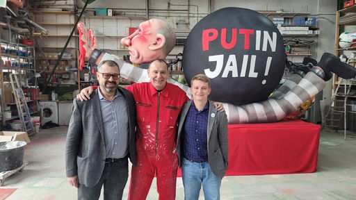 Jacques Tilly und zwei Mitglieder des Vereins Freies Russland NRW stehen Arm in Arm vor der neuen Putin-Figur