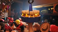 Ein Köbes trägt einen Kölschkranz durch feiernde Karnevalisten in einer Kneipe