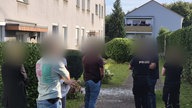 Sechs Leute stehen vor einem Mehrfamilienhaus.