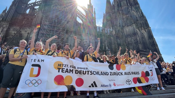 Deutsche Olmypia-Athleten halten eine Fahne mit der Aufschrift: "Team Deutschland zurück aus Paris"