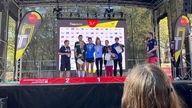 Die Sieger der deutschen Marathonmeisterschaft stehen zusammen einer Bühne und präsentieren ihre Medaillen, Urkunden und Blumensträuße.
