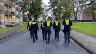 Auf dem Bild sind Polizist*innen von hinten zu sehen, die mitten auf der Straße laufen