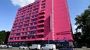 Autos parken vor einem pink angestrichenen Gebäude mit mehreren Stockwerken. 