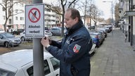 Ein Mitarbeiter des Ordnungsamtes hängt in Krefeld ein Schild auf, das auf das bestehende Alkoholverbot hinweist