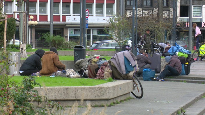 Obdachlose auf dem Krefelder Theaterplatz, daneben viele Säcke und ein Fahrrad mit Decken