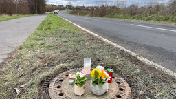 Das Bild zeigt Gedenkkerzen und Blumen auf einem Gully, in dem eine kopfüber steckende Leiche gefunden worden war.