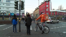 Ein Lieferando-Fahrer steht an einer Kreuzung in Köln.