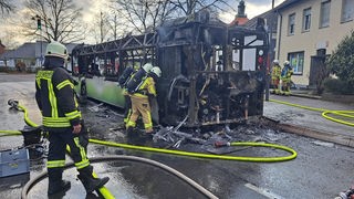 Ein ausgebrannter Linienbus in Kempen, drumherum sind Einsatzkräfte der Feuerwehr zu sehen 