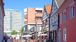 Auf dem Foto ist die Lüner Fußgängerzone: Ein Gasse aus Fachwerkhäusern, an deren Ende ein Hochhaus steht.