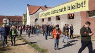 In Lützerath in Nordrhein-Westfalen gehen Demonstranten bei eine Protest-Spaziergang an einem Denkmalgeschütztem Bauernhof vorbei. An dem Bauernhof ist ein großes, gelbes Banner mit dem Aufschrift "1,5 Grad heißt: Lützerath bleibt".