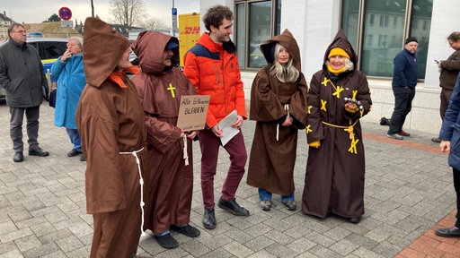 Der Angeklagte mit einer roten Jacke und vier Unterstützern in Mönchskutten vor dem Gericht in Erkelenz