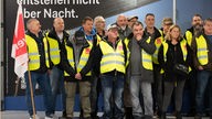Streikende bei der Kundgebung in der Abflughalle am Flughafen Düsseldorf. Sie haben gelbe Warnwesten an, ein Mann links im Bild hält eine Verdi-Fahne in der Hand.