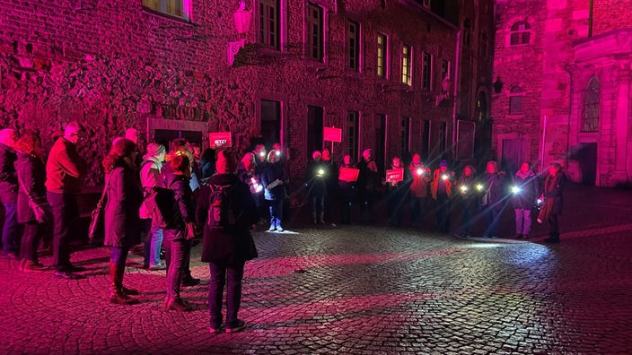 Mehrere Menschen mit Lichtern und Protestplakaten im nächtlichen Domhof