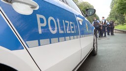 Polizeiauto im Fokus, im Hintergrund Polizisten. 