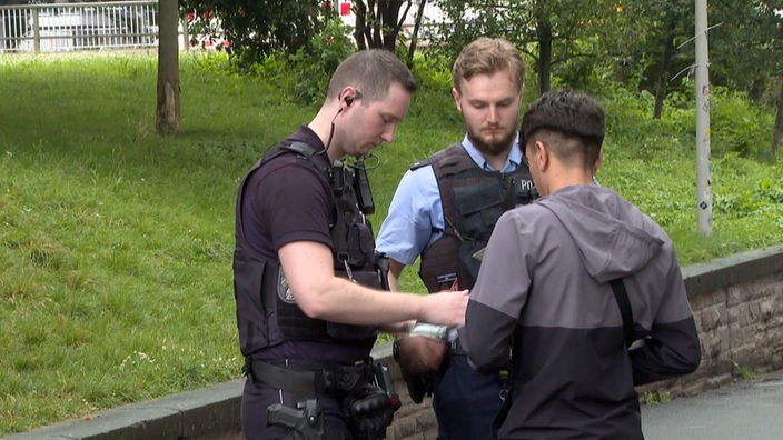 Zwei Polizisten kontrollieren jungen Mann. 