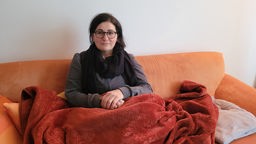 Eine Frau auf einer organgenen Couch mit einer Wolldecke auf dem Schoß