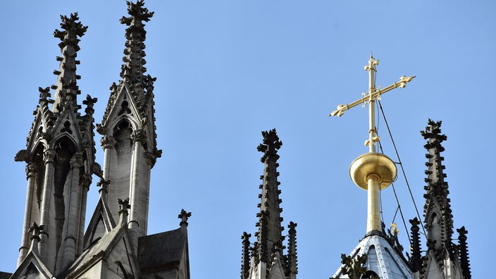 Ein goldenes Kreuz auf dem Kölner Dom leuchtet in der Sonne.