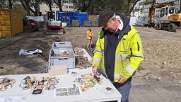 Grabungsleiter Ulrich Karas steht vor einem Tisch und betrachtet ausgegrabene Scherben.