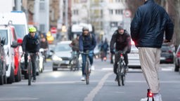 Auf einer Straße fahren mehrere Fahrradfahrer und ein Mann auf einem E-Scooter.