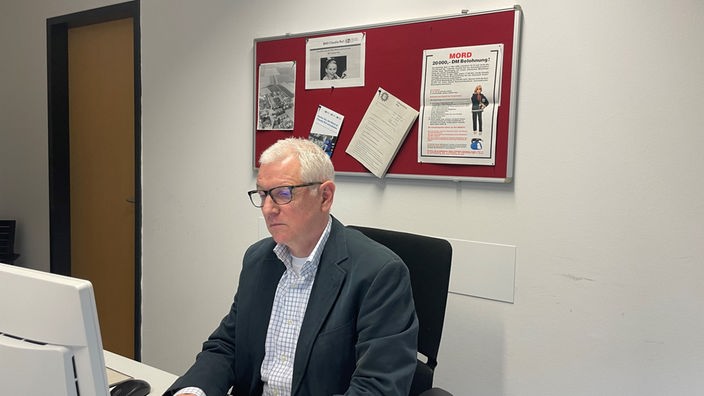 Ein Mann mit grauen Haaren und Brille sitzt am Schreibtisch