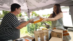 Eine Frau übergibt einer anderen Frau ein orangenes Paket
