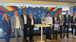 Philipp Lahm und andere Menschen stehen neben dem Euro 24 Pokal
