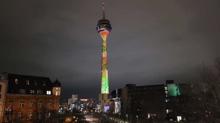 Der Fuß des Rheinturms leuchtet durch eine neue Kunstprojektion in vielen Farben 